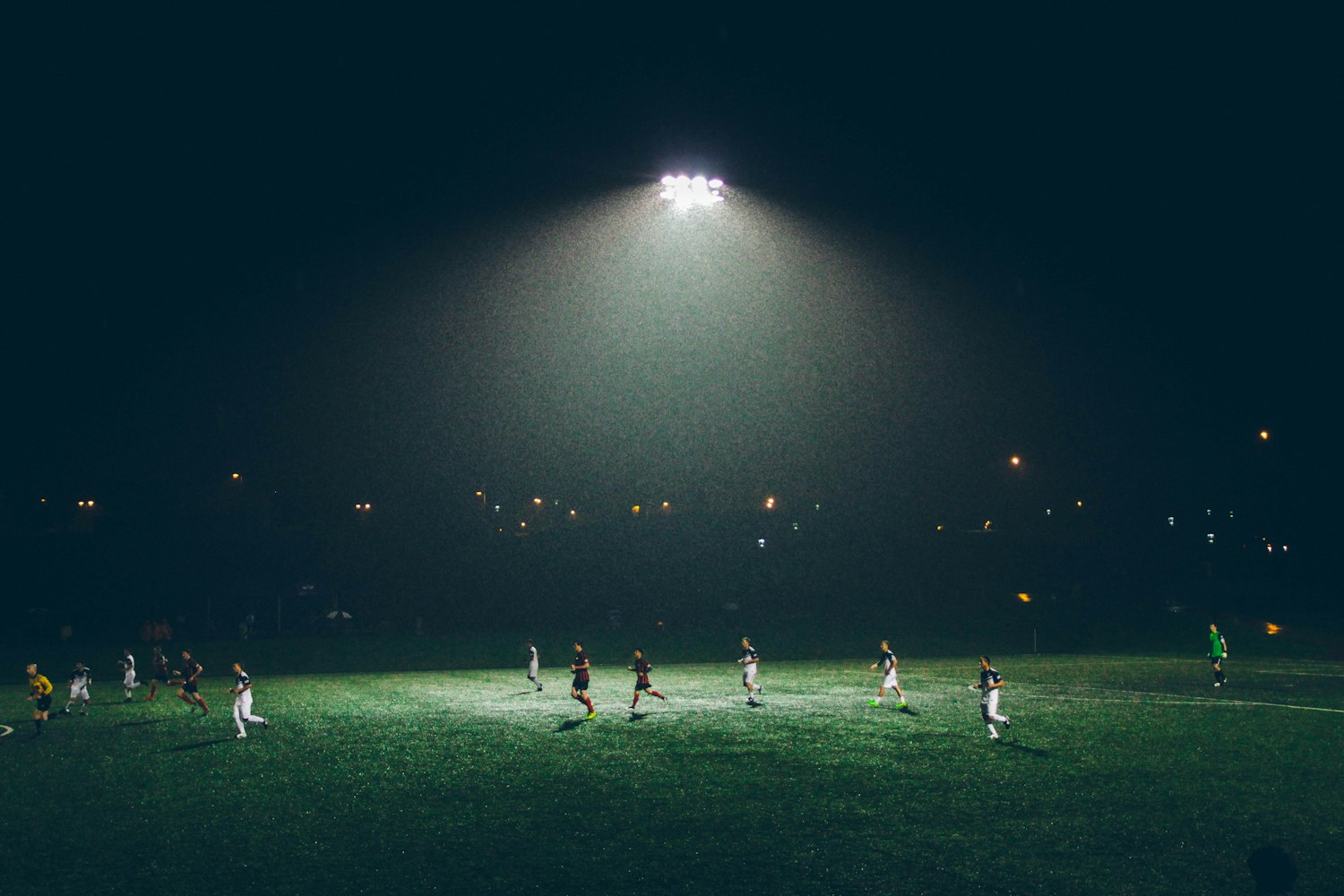 A floodlit pitch at night with the ground beyond