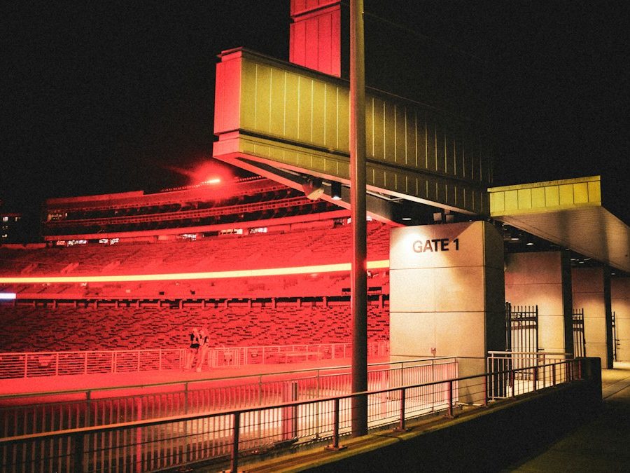 The floodlit exterior of a ground at night, beside its entrance gate